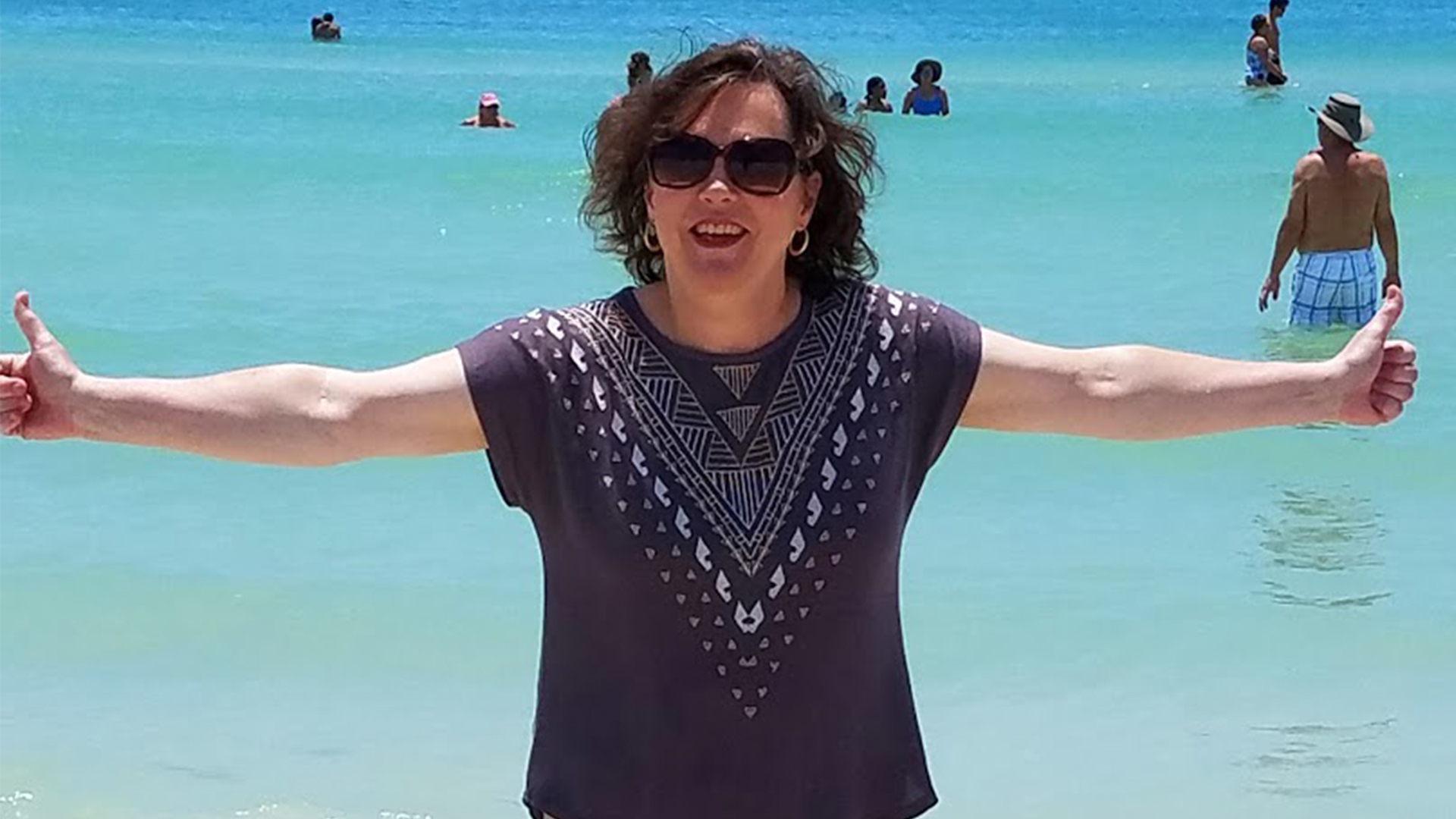 Amy smiling with her arms outstretched at the beach.